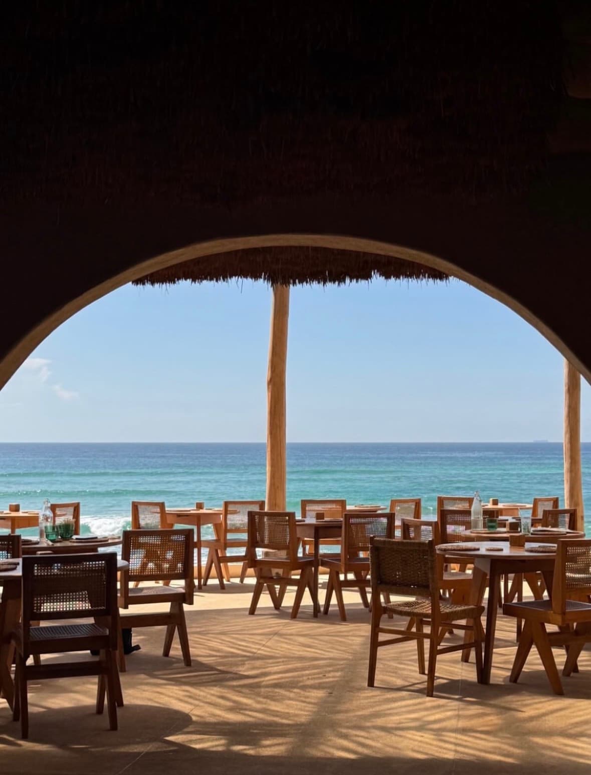 Thatched arch framing tables and the ocean at Kai
