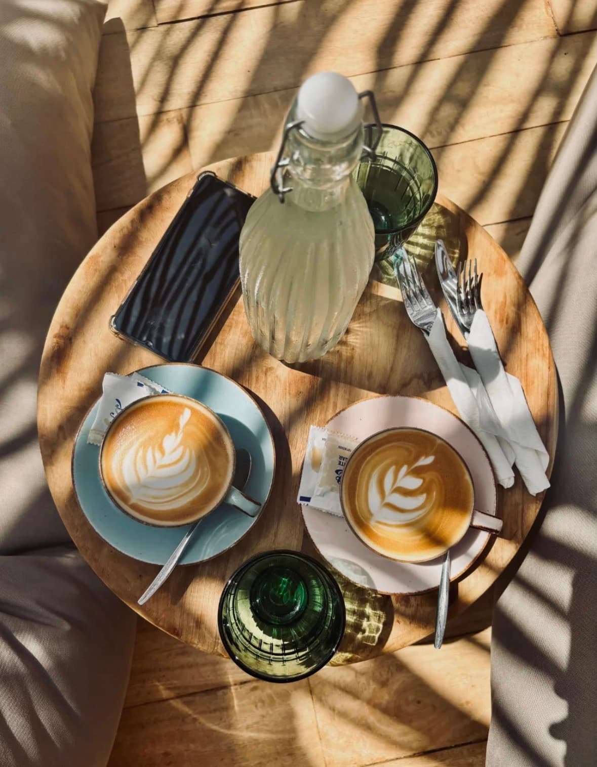 Two coffees with latte art on a round wooden table in the sun