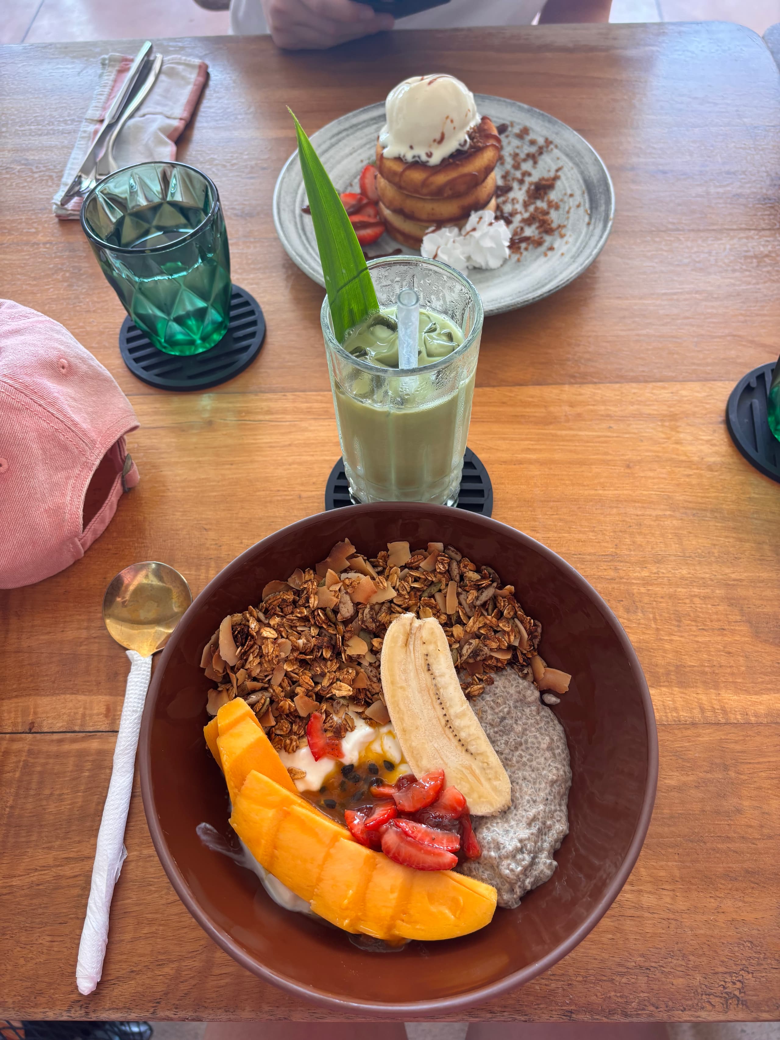 Granola bowl, iced matcha and pancakes on a wooden table