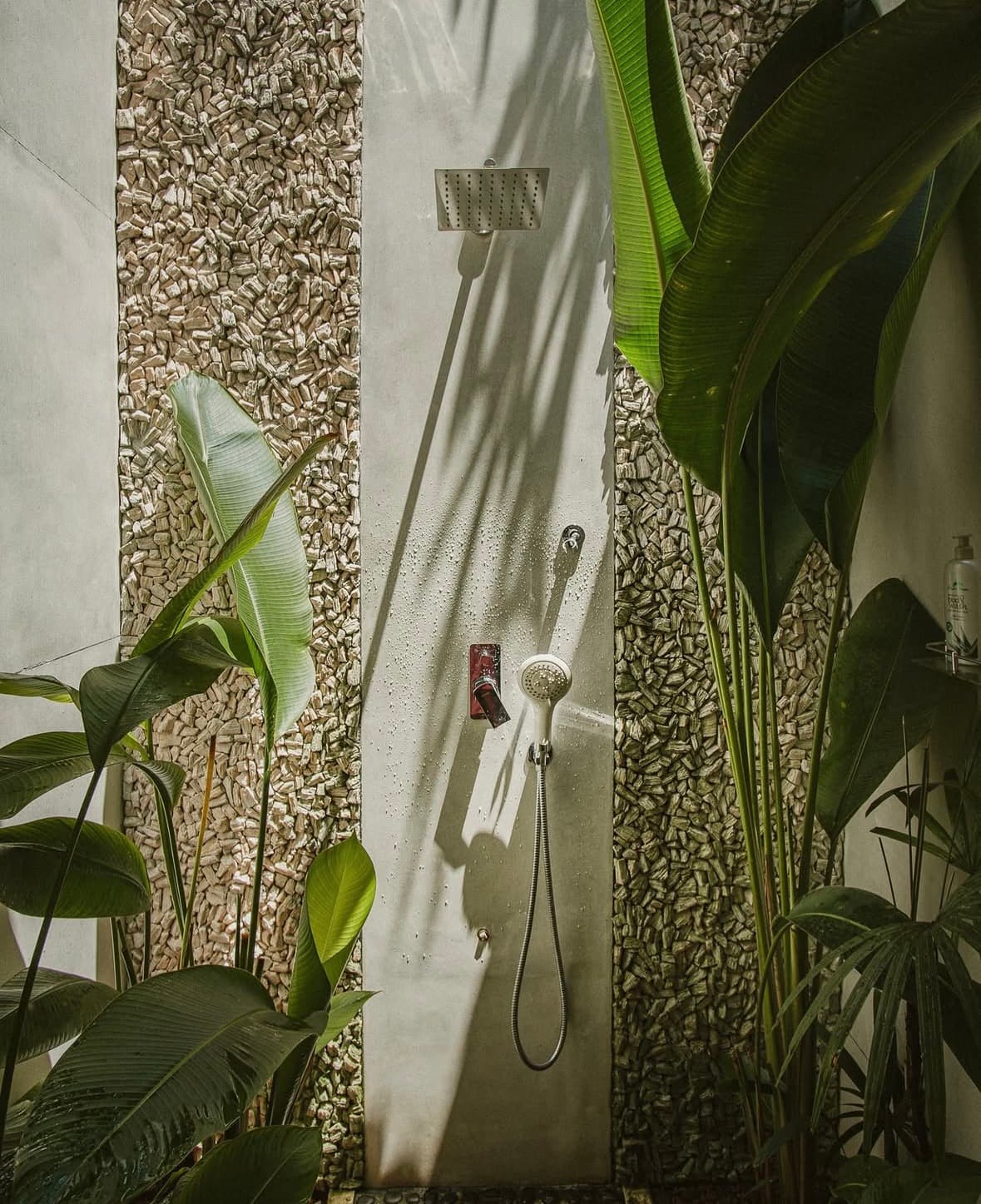 Outdoor rain shower among banana leaves and pebble walls